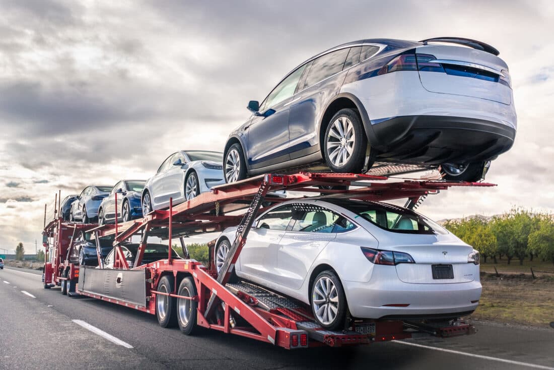 Red open car carrier loaded with electric SUVs on the open road